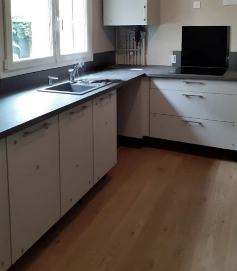 Cuisine moderne en cours d'installation avec éléments bas blancs en L, plan de travail gris foncé, évier inox encastré et robinet mitigeur